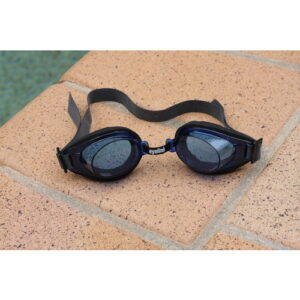 black pair of eyeline deluxe swim goggles laying on tiles next to a pool